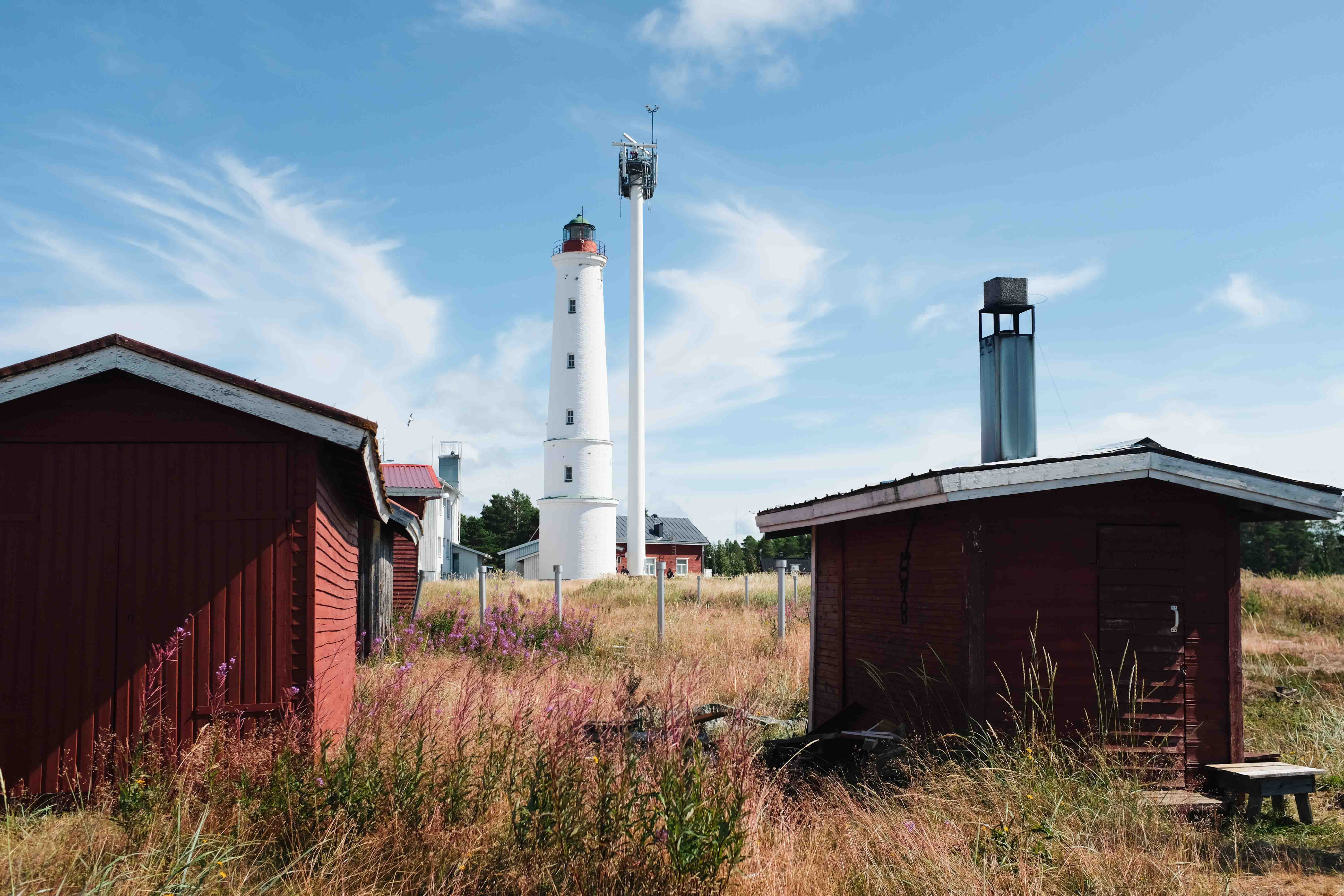 A white lighthouse surrounded by wooden red houses.